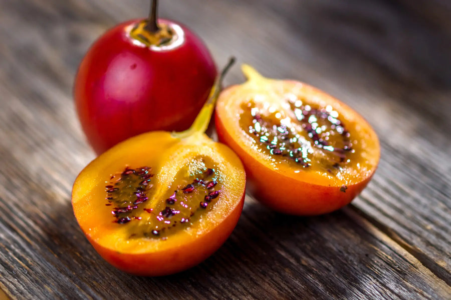 Aufgeschnittene Tamarillo mit gelbem Fruchtfleisch und dunklen Samen auf Holztisch.
