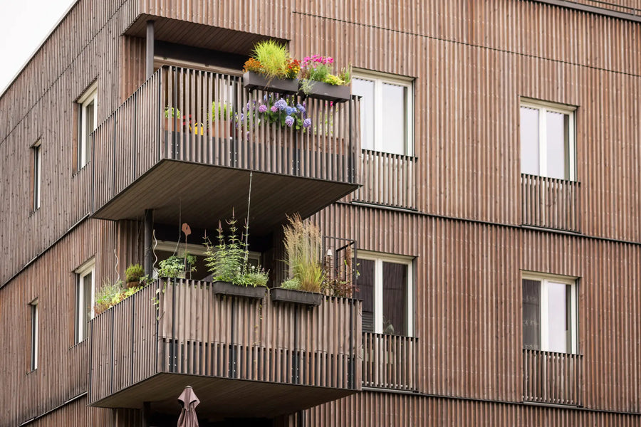 Moderner Balkon mit Windschutz und bepflanzten Blumenkästen an Holzfassade.