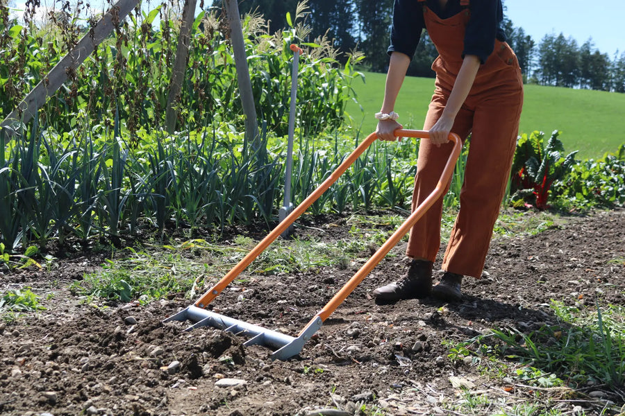 Person lockert Gartenboden mit einer Broadfork auf einem Gemüsebeet.